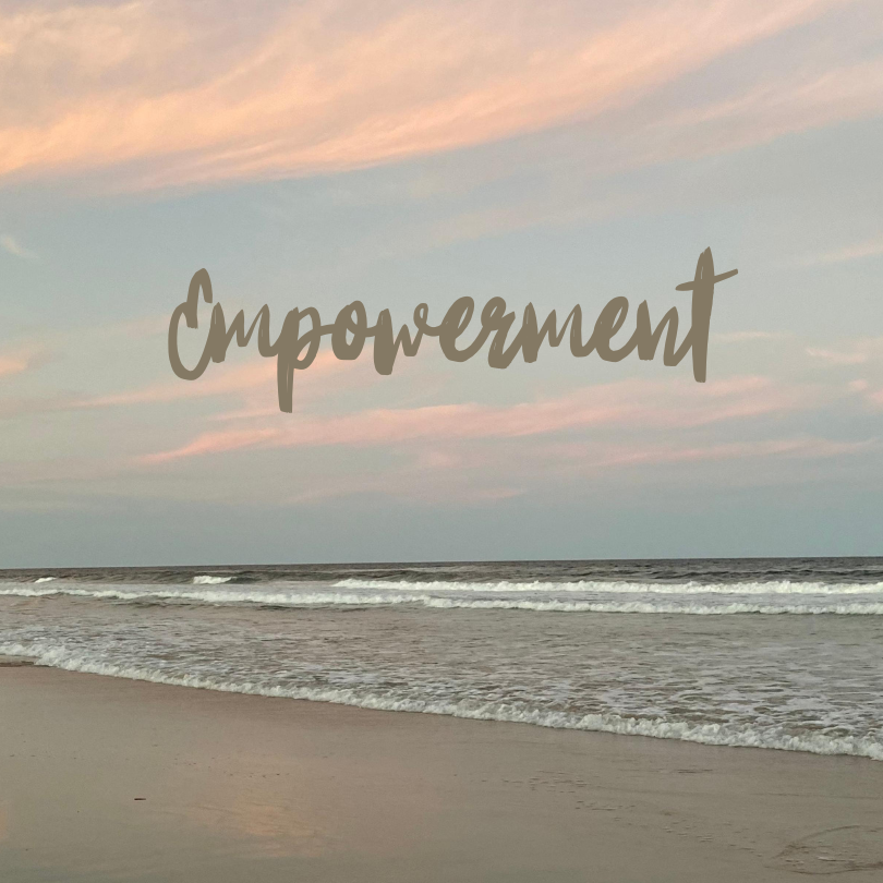 The word 'empowerment' is documented on a beach at sunset.