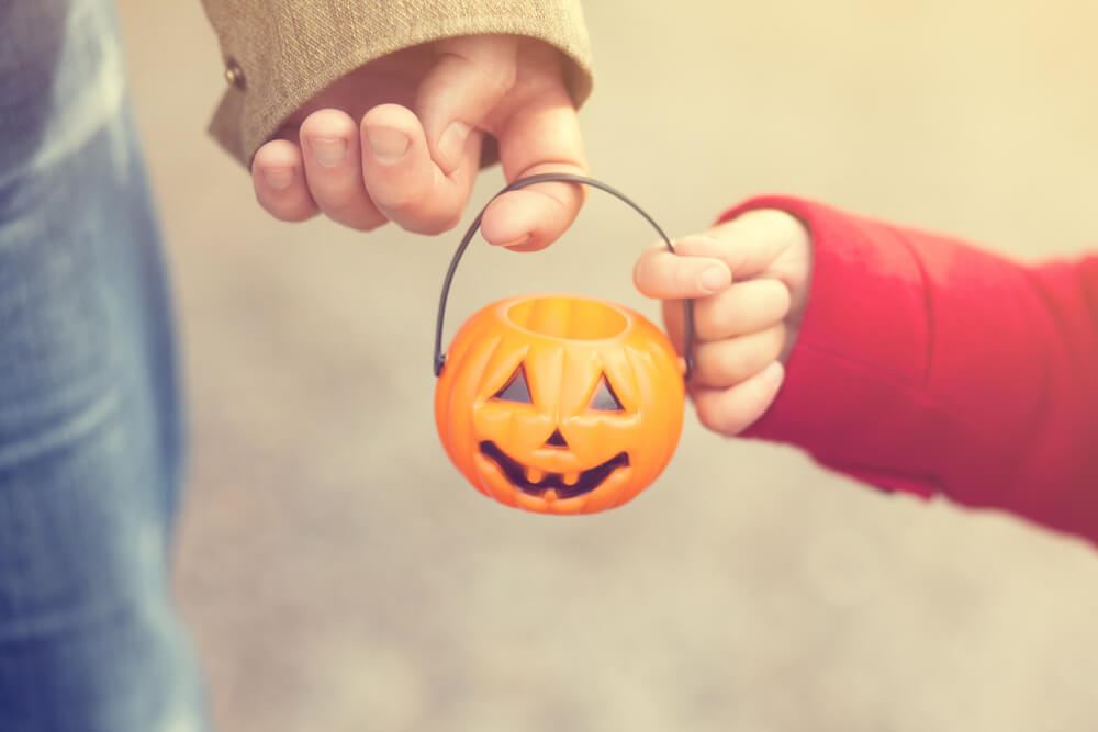 A child holding a jack-o-lantern, embracing the Halloween traditions with their co-parent.