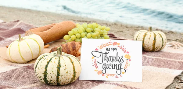 A Thanksgiving card with pumpkins on a blanket on the beach.