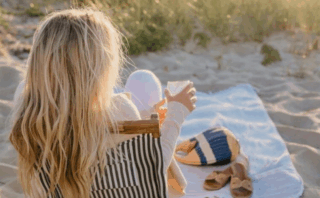 A woman sits on a striped beach chair on sand, holding a cup, with a hat and bag beside her. Overlaid text reads: “Documenting Abuse” – sharing my experiences documenting abuse on the Divorce Diaries Podcast.
